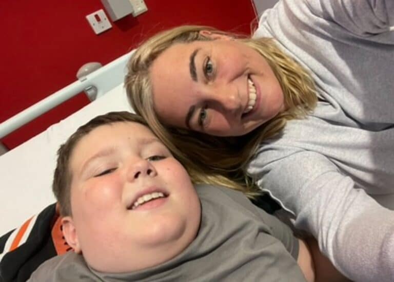 Oliver and his mum Anna laying on a bed smiling at the camera