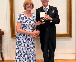Bobbie Nichols shaking hands with Lord Lingfield, President of the League of Mercy, and holding order of mercy award medal