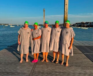 Team of five people in swimming hats with and towels infront of a lake