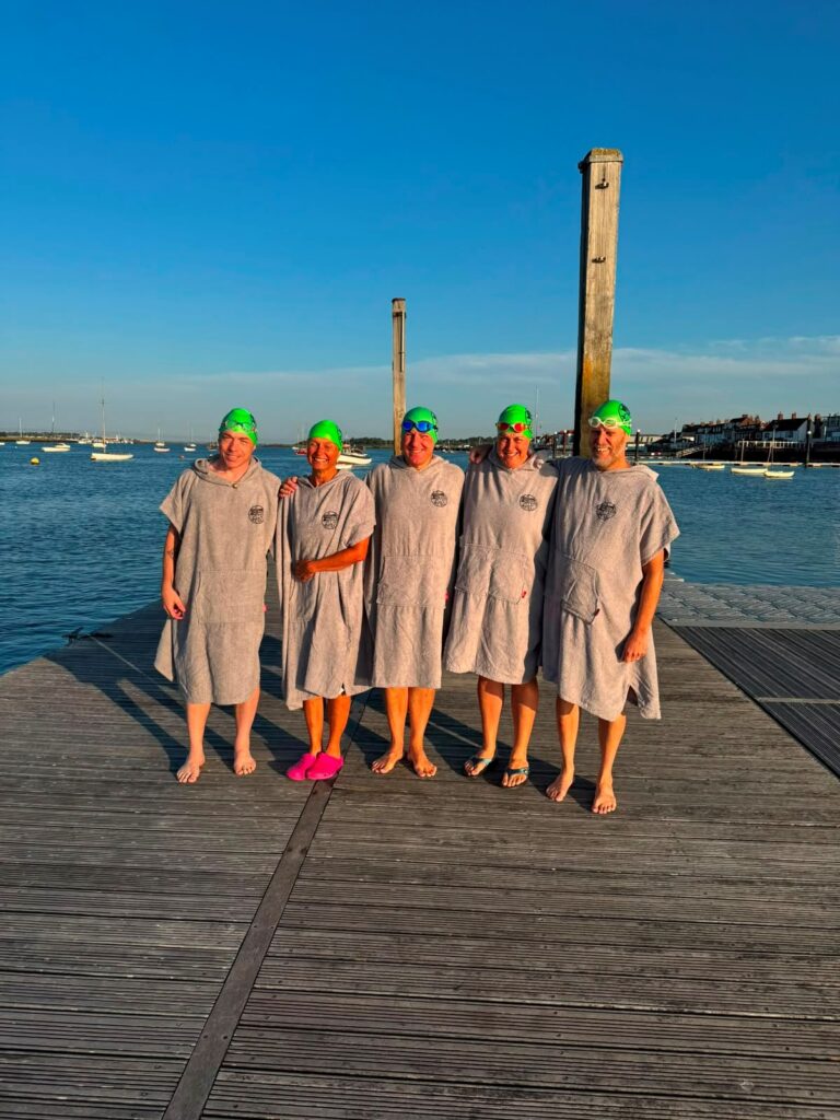 Team of five people in swimming hats with and towels infront of a lake