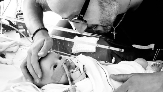 small baby in hospital cot with dad looking down at him the photo is black and white