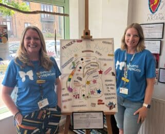 Two women wearing Havens Hospices tops standing next to an easel with a canvas on it.