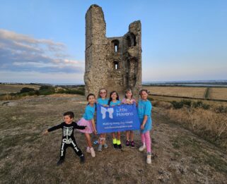 Five young girls and one young boy dressed in colourful outfits in front of Hadleigh Castle