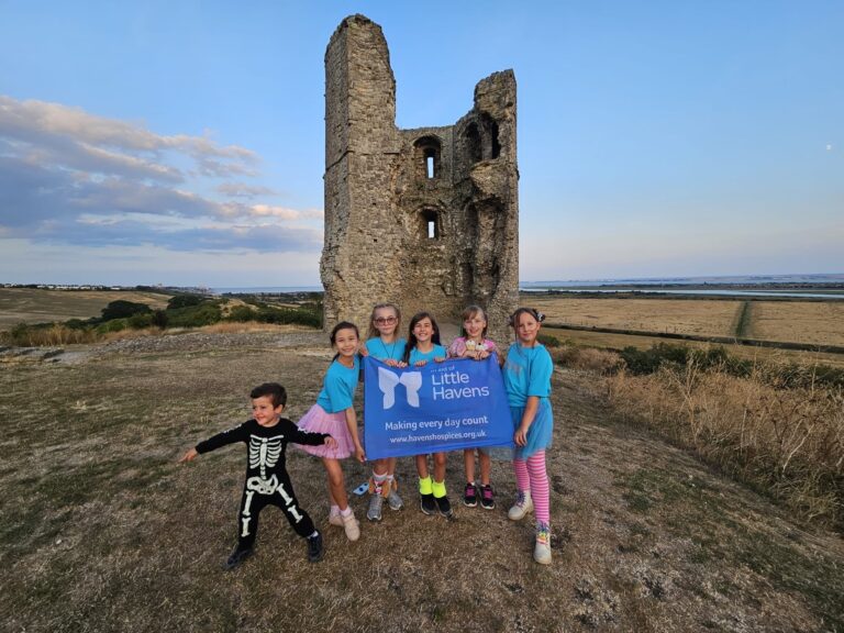 Five young girls and one young boy dressed in colourful outfits in front of Hadleigh Castle