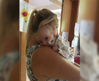 Baby held up to mum's shoulder looking at the camera