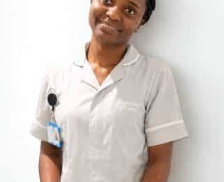 Emmanuela, student nurse, in her uniform, standing in front of a white wall