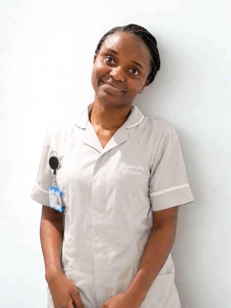 Emmanuela, student nurse, in her uniform, standing in front of a white wall