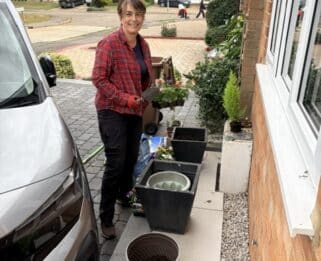 A lady smiling on someones driveway doing gardening.