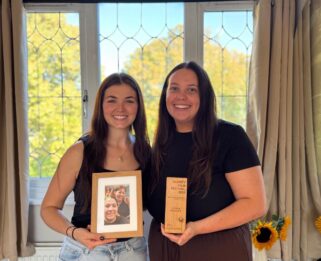 Two women smiling one holding a photo the other holding a trophy