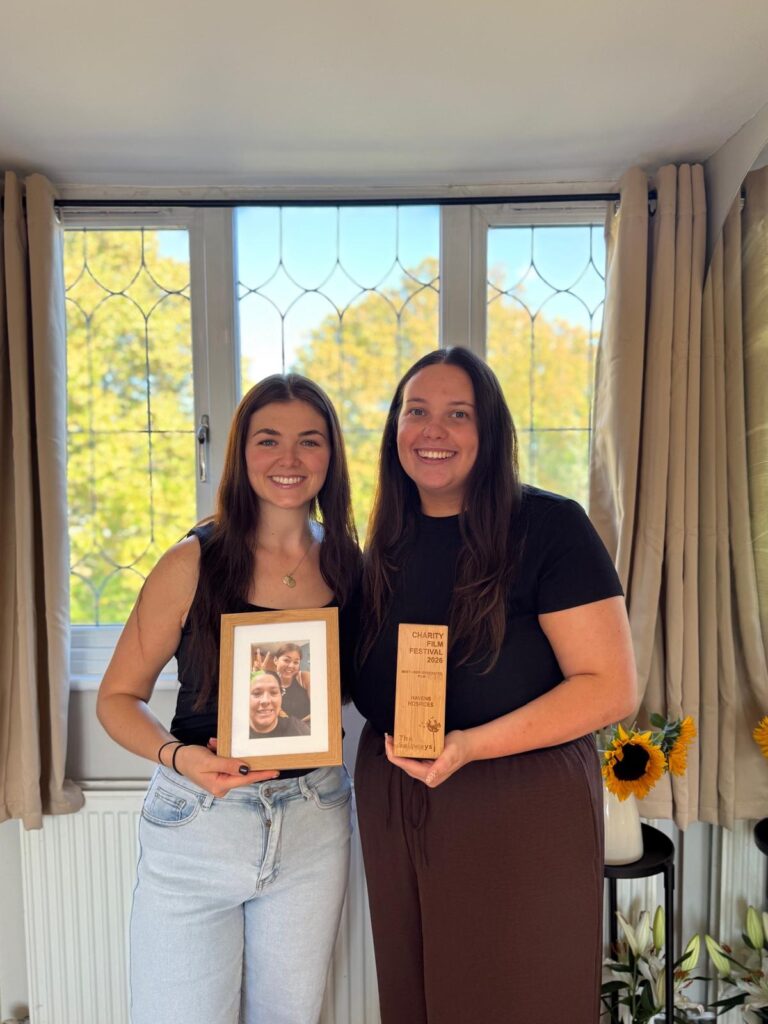 Two women smiling one holding a photo the other holding a trophy